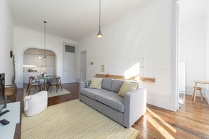 Un salon moderne avec un canapé gris, un plancher en bois et un coin repas comprenant une table et des chaises.