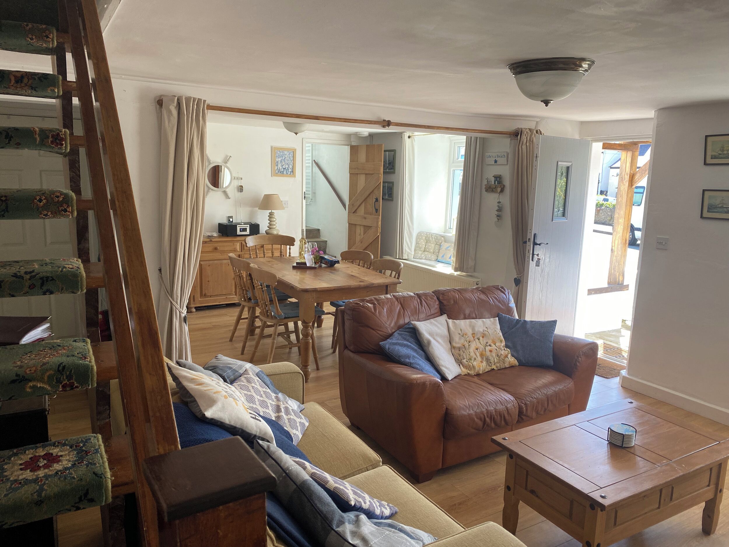 A cozy living room with a brown leather sofa, a wooden coffee table, and a dining area with a wooden table and chairs.