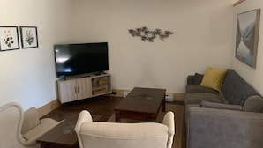 Una sala de estar con un televisor de pantalla plana, un sofá, una mesa de centro y una silla.