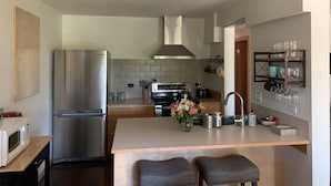 Una cocina moderna con un refrigerador de acero inoxidable, horno empotrado e isla central con dos taburetes.