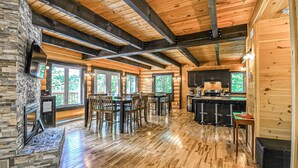 Ein geräumiges Blockhaus-Interieur mit Kamin aus Stein, Essbereich aus Holz und einer Küche mit Bar.