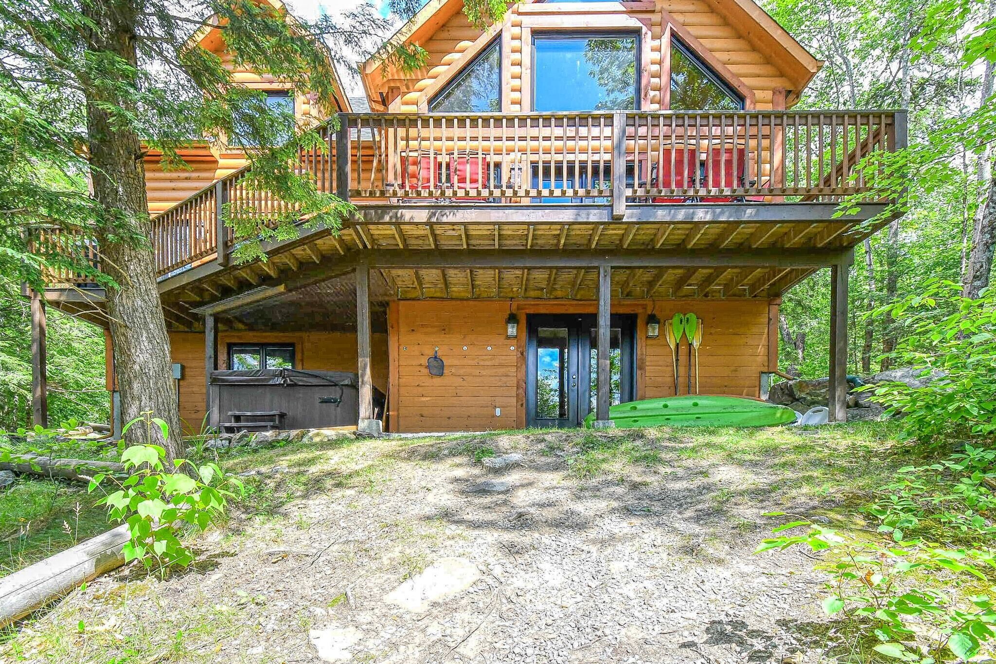 A cabin with a wooden exterior, a balcony with red chairs, and a green outdoor area.