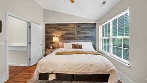 Ein Schlafzimmer mit einem Bett, einem Nachttisch, einer Lampe, einem Deckenventilator und einem Fenster mit Jalousien.