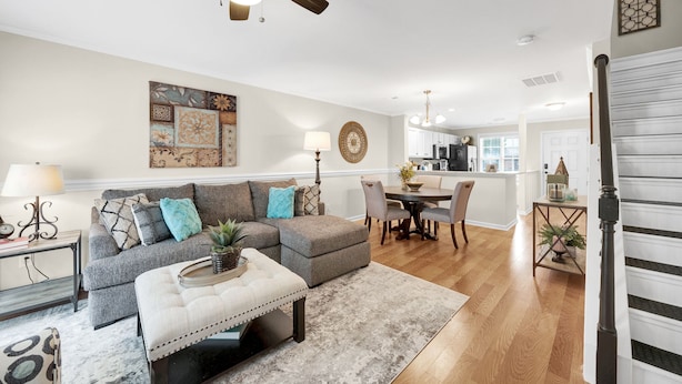 Ein modernes Wohnzimmer mit einem grauen Ecksofa, einem weißen Pouf und einem Essbereich mit einem Holztisch und Stühlen.