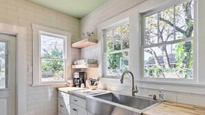 A kitchen with white cabinets, a stainless steel sink, wooden countertops, and large windows with a view of trees.