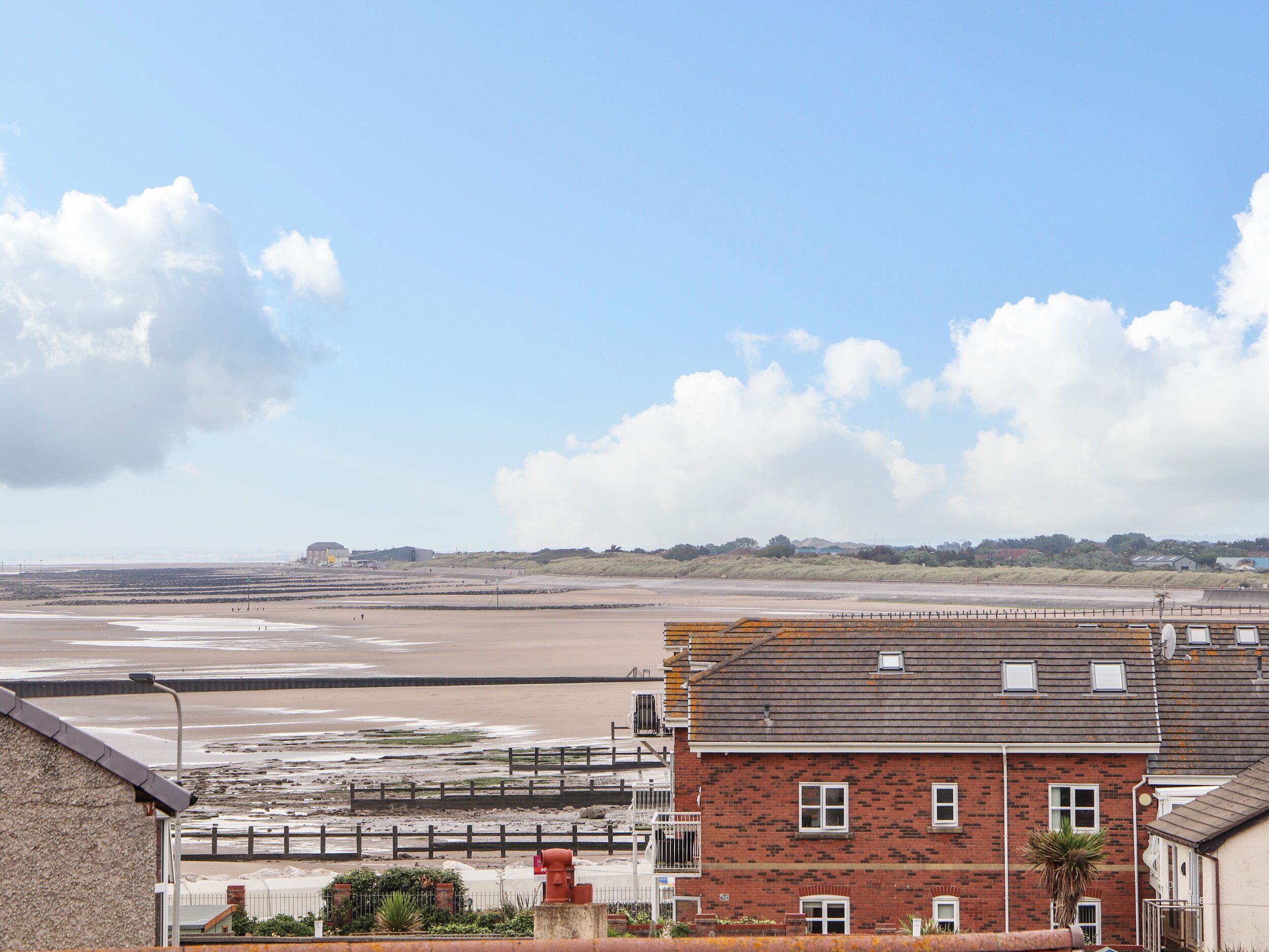 A coastal building with a brick facade, a flat roof, and a visible balcony.