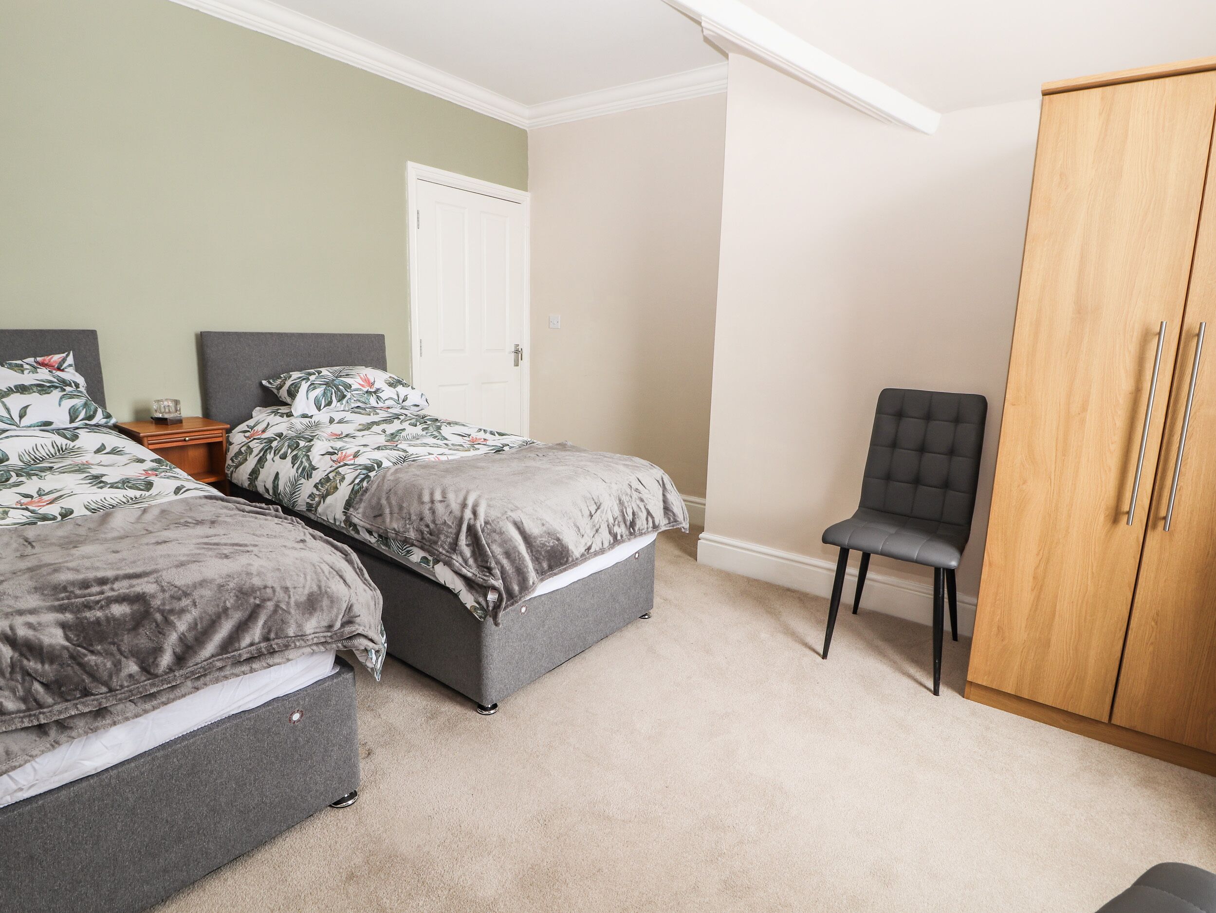 A bedroom with two beds, a wardrobe, a chair, and a door.