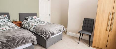 A bedroom with two beds, a wardrobe, a chair, and a door.
