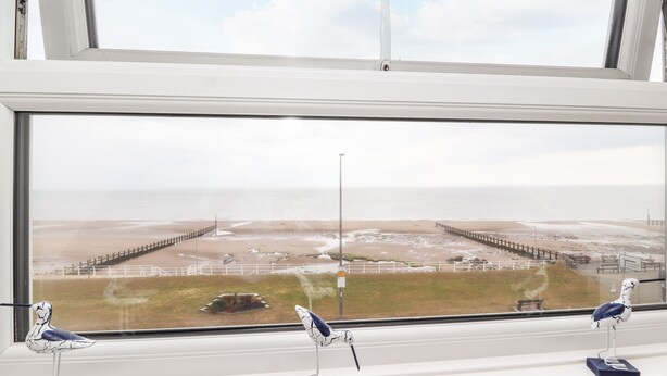 A window with a view of a beach and a pier. There are three bird figurines on the windowsill. - Ty Uchaf (Rhyl)