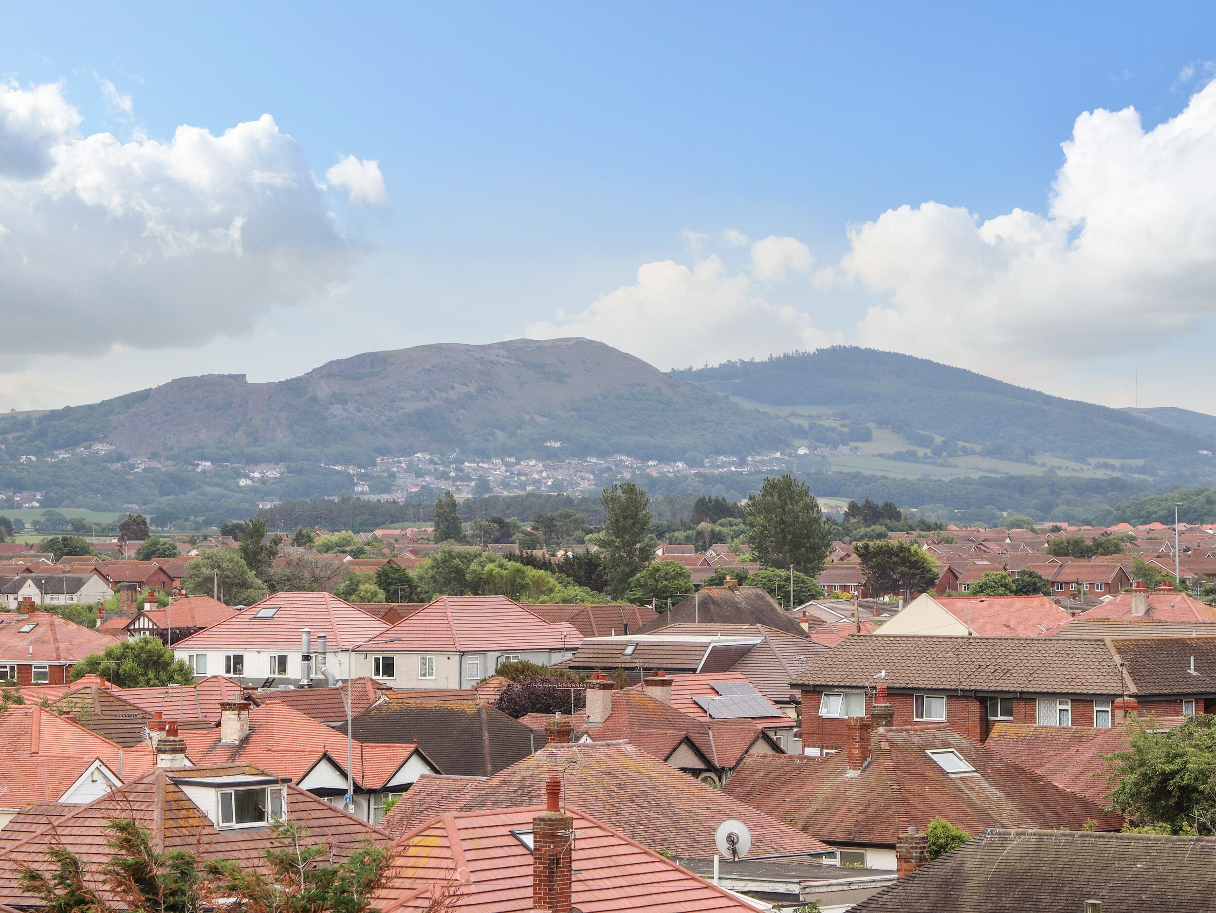 A residential area with red-tiled roofs, houses, and a mountain in the background.