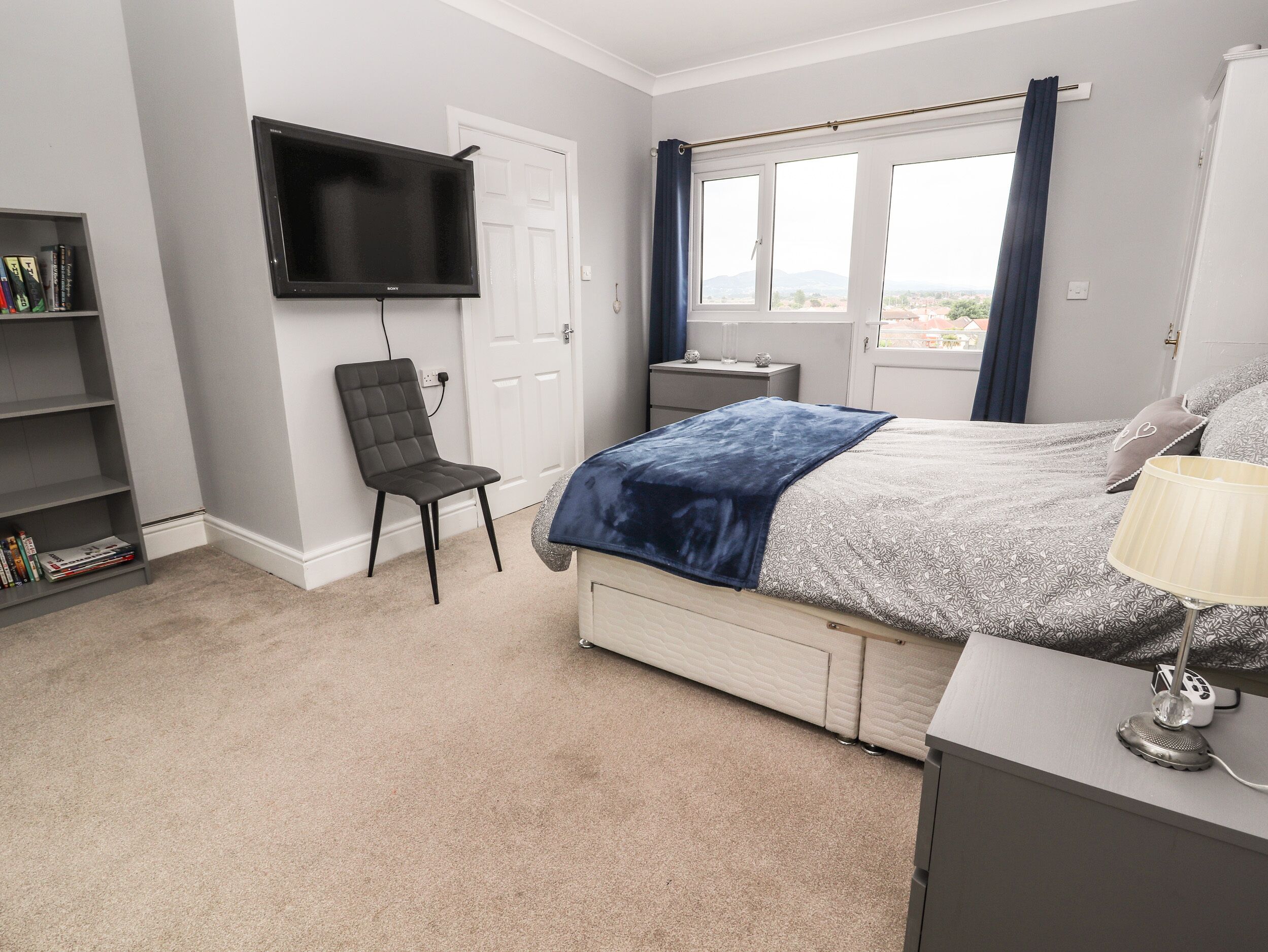 Une chambre à coucher avec un lit, une chaise, un téléviseur, un bureau et une bibliothèque.