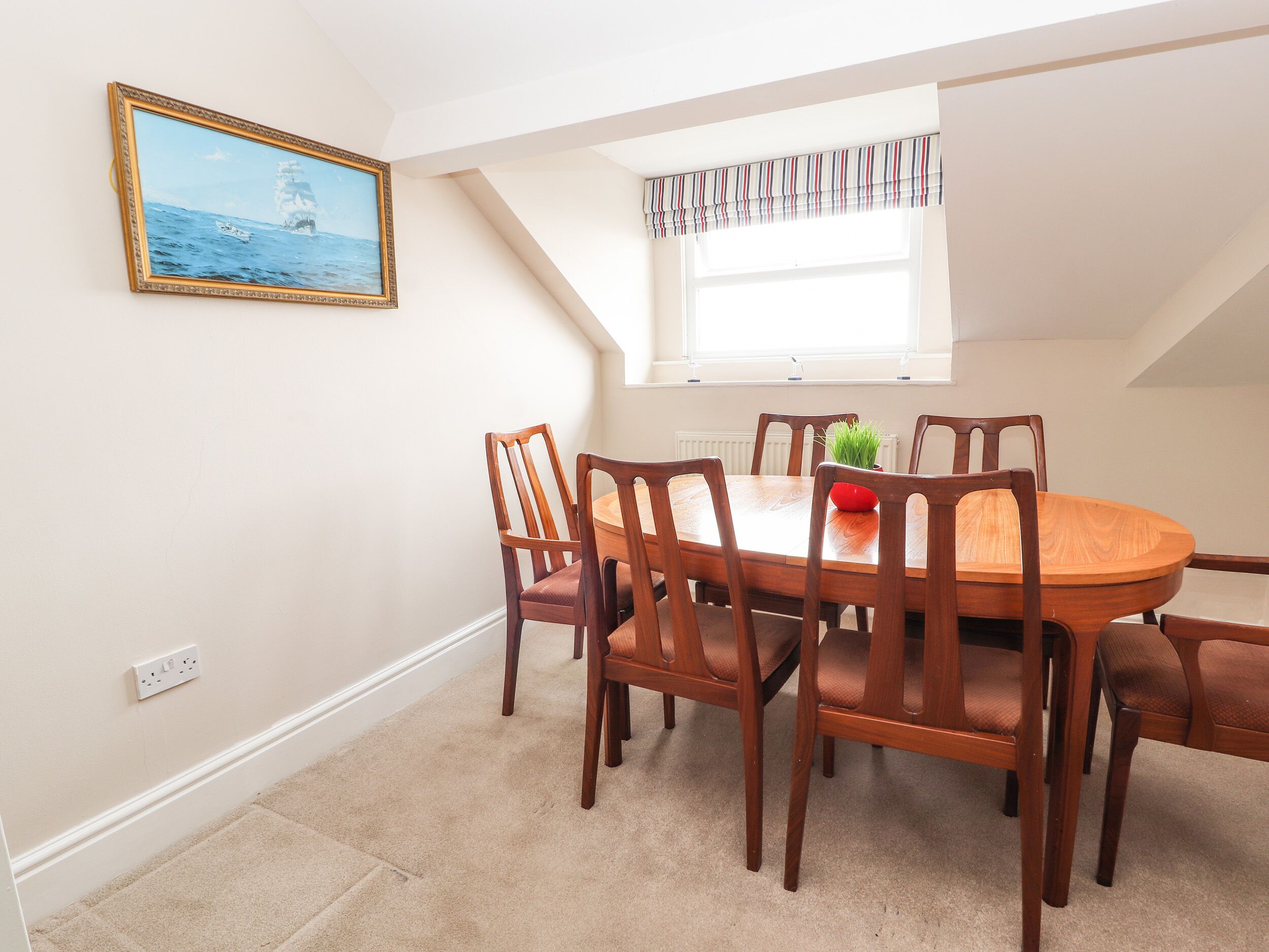 A dining area with a wooden table and chairs, a painting on the wall, and a window with a striped valance.