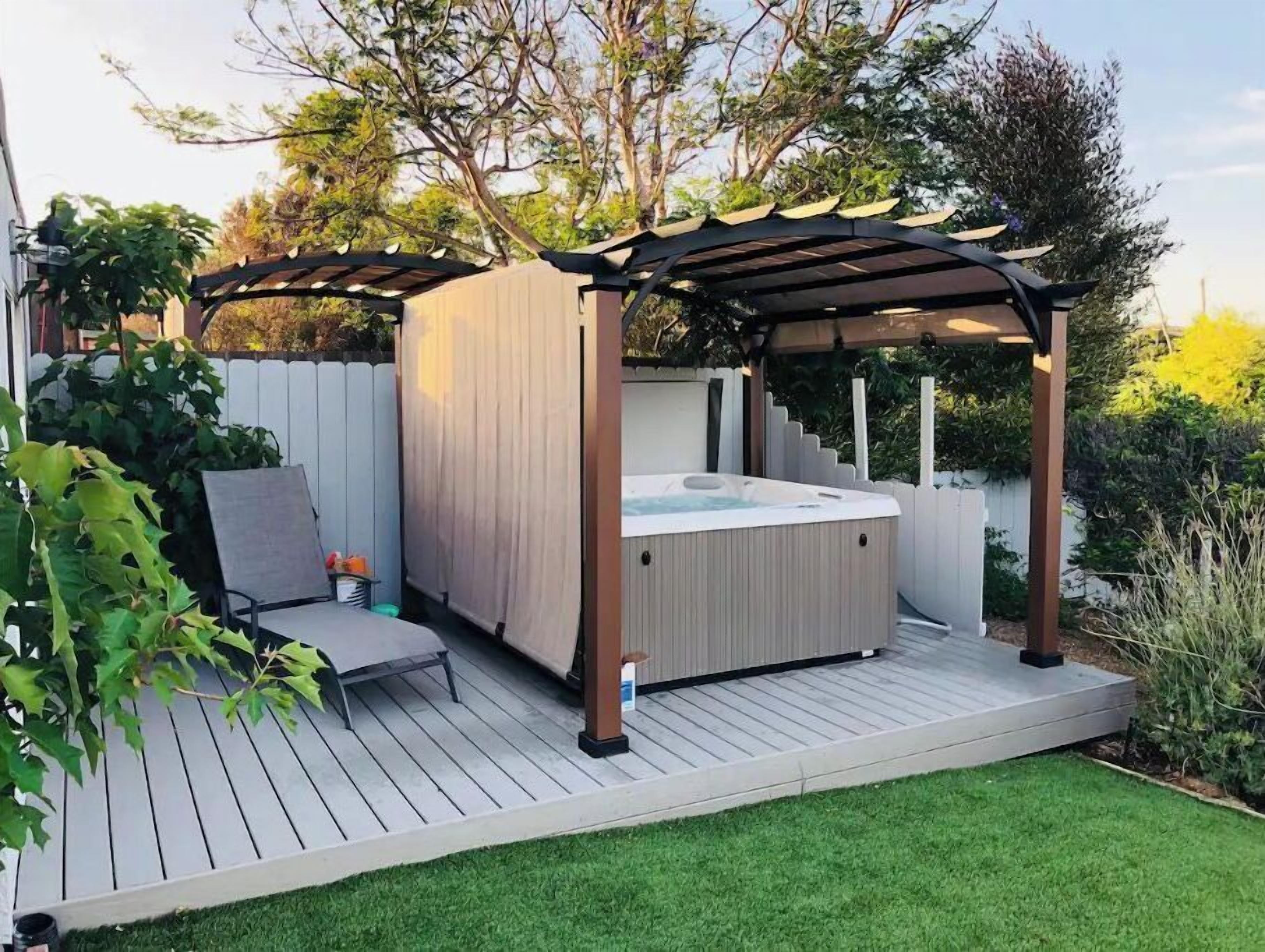 A hot tub under a pergola on a wooden deck with a grassy lawn.