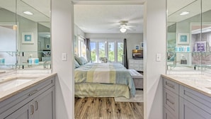 A bedroom with a large bed, a ceiling fan, and a view of the outdoors through a window. - Longboat Key Cedars Beach House (Longboat Key)