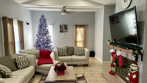 A living room with a Christmas tree, sofas, a coffee table, a fireplace with stockings, and a TV.