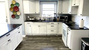 A kitchen with white cabinets, a black countertop, a window, and a microwave.