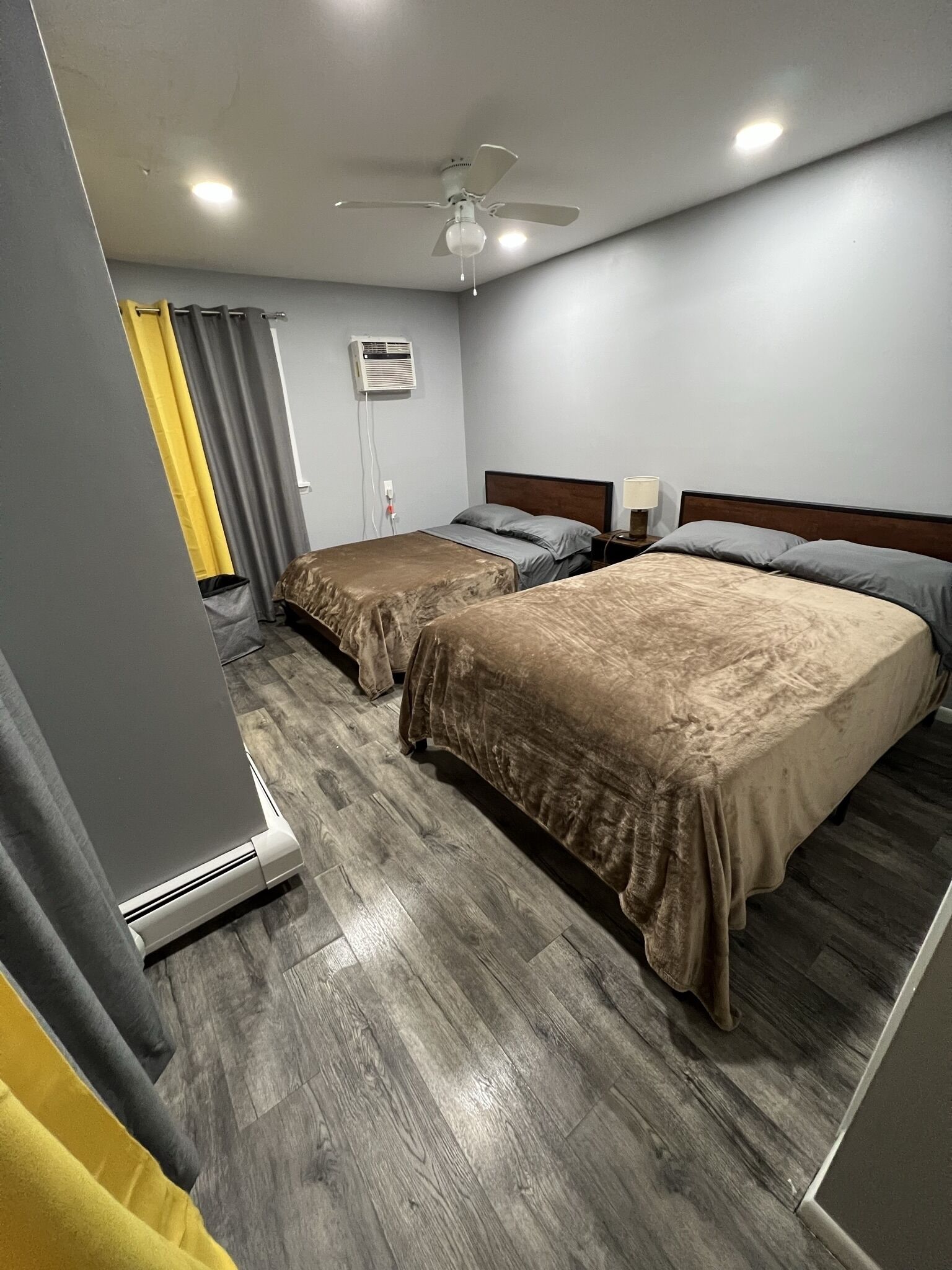 A hotel room with two beds, a ceiling fan, an air conditioning unit, and a wooden floor.