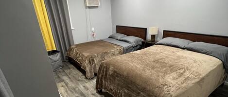 A hotel room with two beds, a ceiling fan, an air conditioning unit, and a wooden floor.