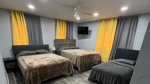A hotel room with two beds, a ceiling fan, a TV, and wooden flooring.