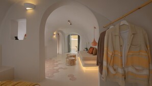 A modern hotel room with a minimalist design, featuring an arched doorway, a seating area with cushions, and a hanging coat rack. - Elements Cave Suites (Santorini)