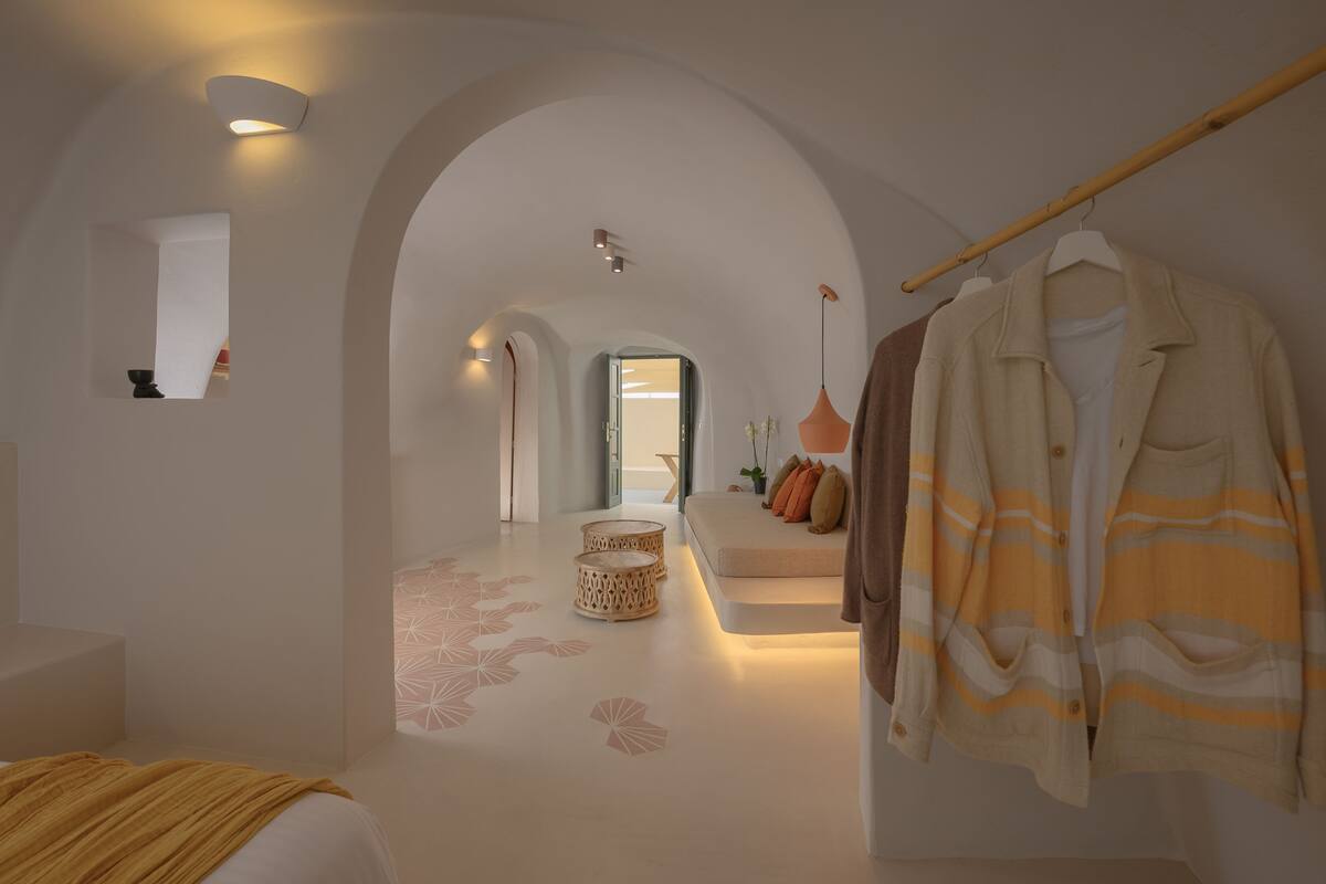 Habitación de hotel moderna con un diseño minimalista, que incluye un arco de entrada, una zona de estar con cojines y un perchero colgado.