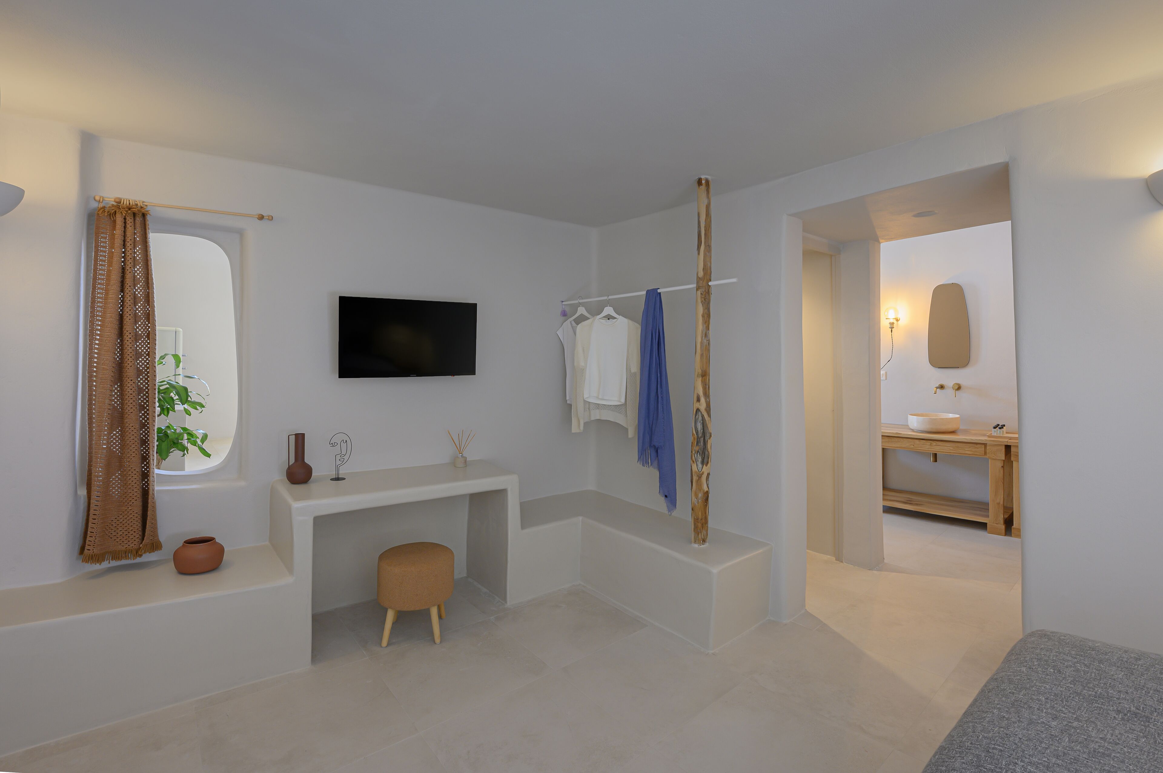 A modern bathroom with a white vanity, a flat-screen TV, a towel rack, and a wooden bench.