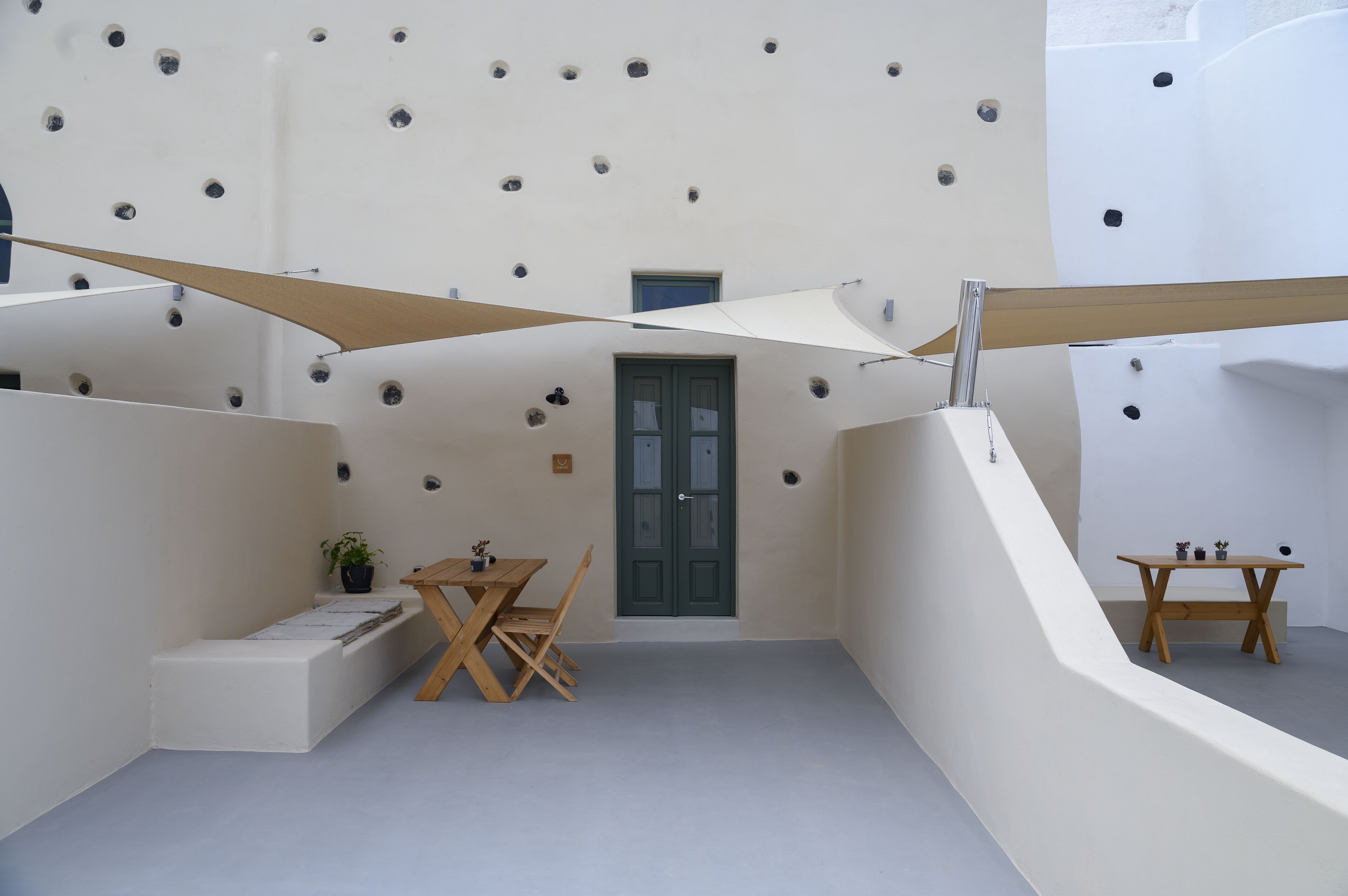 Ein modernes Interieur mit minimalistischem Design, das einen Holztisch und Stühle, einen kleinen Topfpflanzen und eine Tür mit grünem Rahmen zeigt.