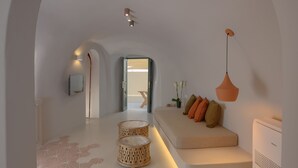 A modern interior with a high arched doorway, a sofa with cushions, a small table, and a hanging light fixture. - Elements Cave Suites (Santorini)
