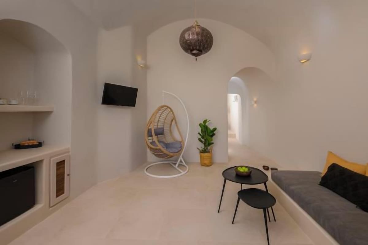 Un salon moderne avec un canapé, un fauteuil suspendu, une petite table et un téléviseur fixé au mur.