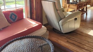 A cozy room with a wooden ceiling, a leather chair, a cushioned bench, a glass table, and a wall-mounted air conditioner.