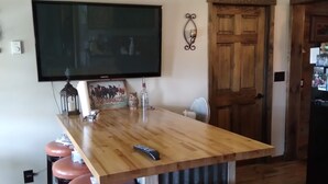 A kitchen with a wooden island, bar stools, a flat-screen TV, and a ceiling fan.