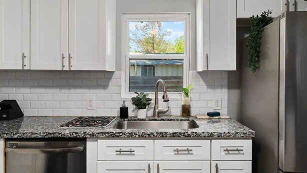 A kitchen with white cabinets, a granite countertop, stainless steel appliances, and a window with a view of a tree and a building. - Spacious Patio + Close to The Square + Pet Friendly + Full Kitchen (San Marcos)