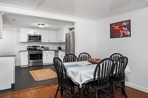 Ett modernt kök med vita skåp, rostfria vitvaror och en matplats med svarta stolar och ett vitt bordsduksöverdrag.