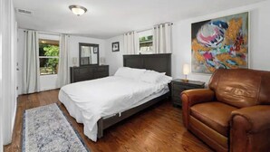 A bedroom with a bed, a brown leather chair, a nightstand, a painting, and a window with curtains. - Spacious Patio + Close to The Square + Pet Friendly + Full Kitchen (San Marcos)
