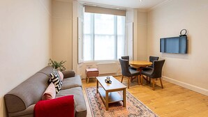 A modern living room with a grey sofa, red cushion, wooden coffee table, and a dining area with chairs and a table.
