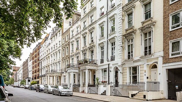 A row of traditional white townhouses with uniform architecture, a sidewalk, and parked cars.