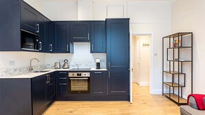 A modern kitchen with dark cabinetry, a built-in oven, and a marble countertop.