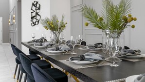 A modern dining room with a long table, dark chairs, and a unique chandelier.