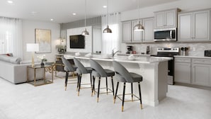 A modern kitchen with white cabinetry, a central island with bar stools, a built-in microwave, and a large window.