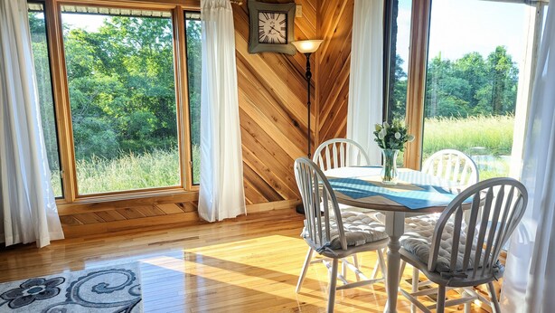 A dining area with a wooden ceiling, large windows with curtains, a table with chairs, and a clock on the wall. - A Romantic Getaway on the Bourbon Trail (Willisburg)
