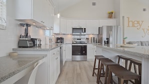 A modern kitchen with white cabinets, stainless steel appliances, and a granite countertop. - Beachfront Retreat l Hot Tub l Gulf Views, Wraparound Deck, Sleeps 12, Pet-Friendly, & More (Gilchrist)