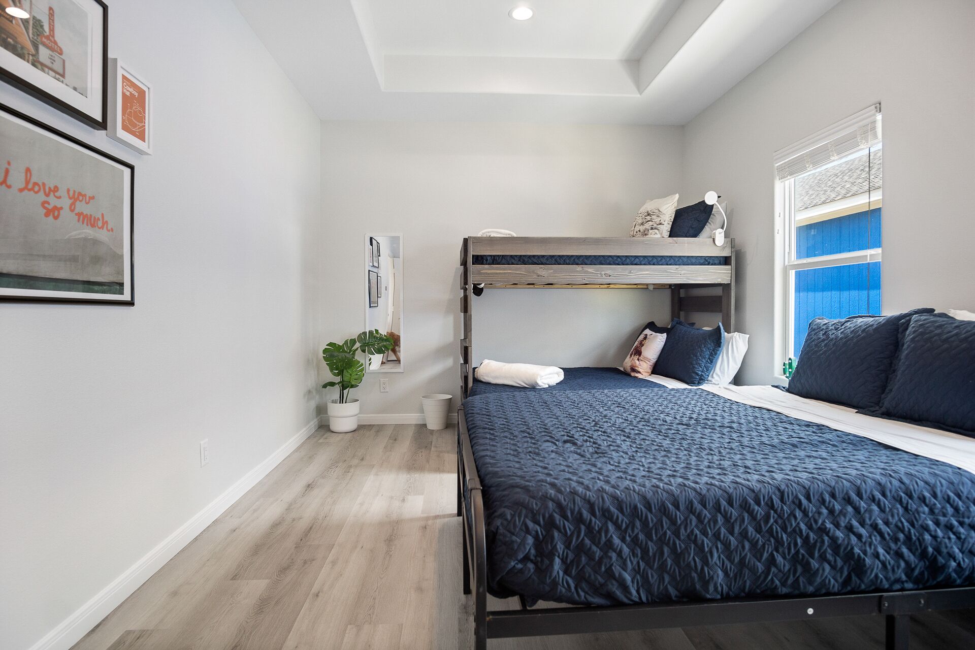A bedroom with a bunk bed, a large bed, a potted plant, and framed pictures on the wall.