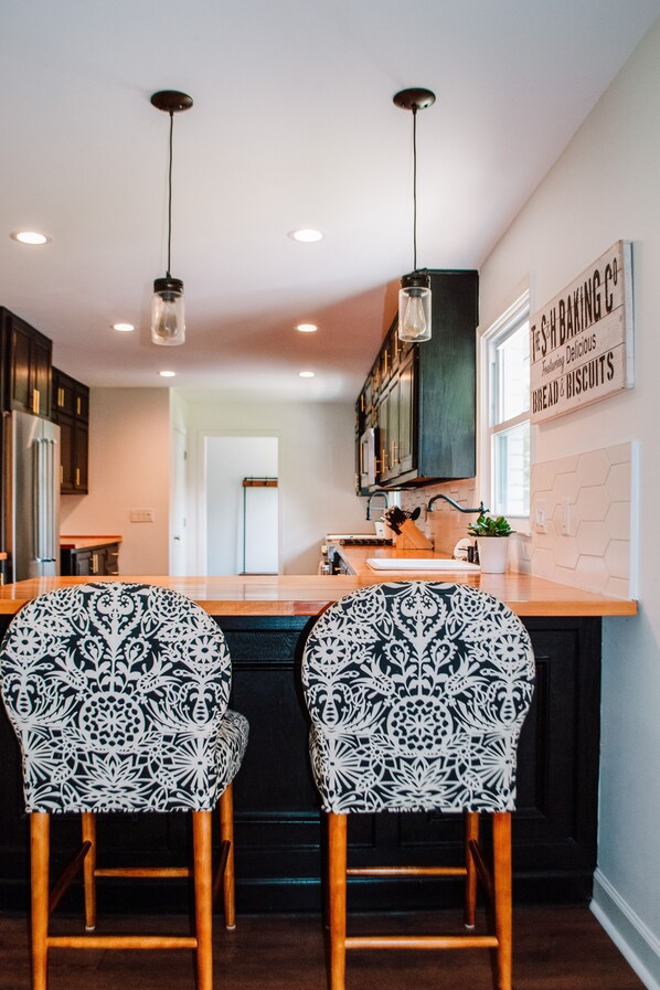 A kitchen with two patterned chairs, a wooden countertop, and pendant lights.