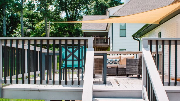 Une terrasse en bois avec une balustrade blanche, une structure de jeux verte et une maison blanche en arrière-plan.
