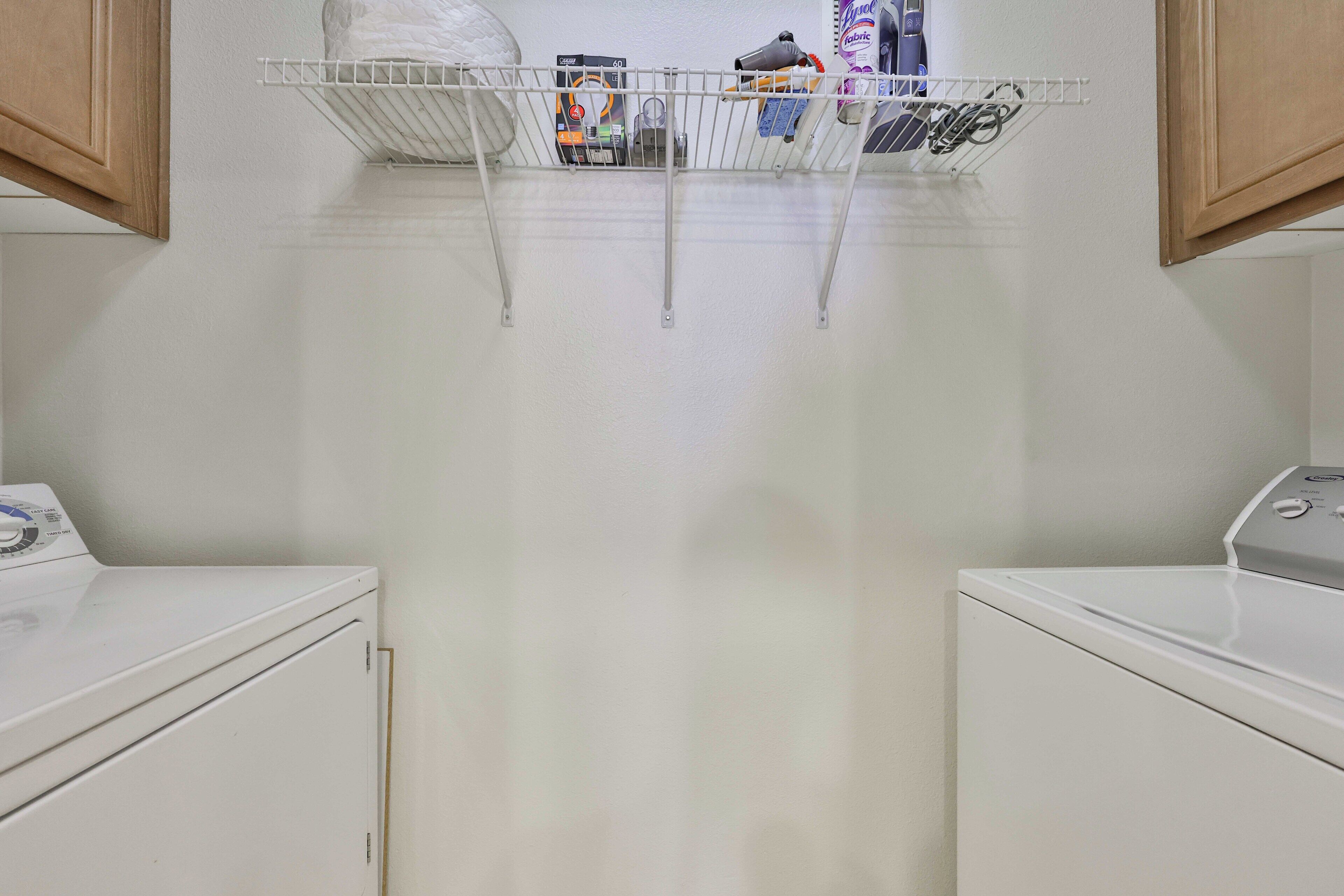 A laundry area with two white washing machines, a metal drying rack with folded clothes, and a shelf with laundry supplies.
