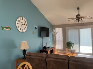 Uma sala de estar com sofá, relógio, televisão e ventilador de teto.