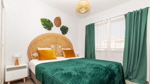 A bedroom with a bed, green curtains, a white nightstand, and a wall-mounted lamp.