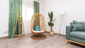 A living room with a green sofa, a wicker chair, a floor lamp, a potted plant, and a ladder against the wall.