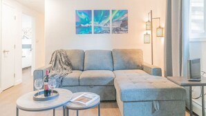Een moderne woonkamer met een grijze modulaire bank, een klein rond tafeltje met een wijnglas en een boek, en een tv op een dressoir.