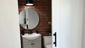 A modern bathroom with a white sink, round mirror, and toilet. - Mountain Views/Studio in Montecito. 7-10 min to beach or downtown SB (Montecito)